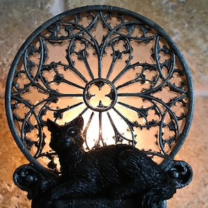 Peut inclure: Une veilleuse en forme de chat noir avec un motif de vitrail. La lumi&egrave;re est allum&eacute;e et le chat est assis devant le vitrail.