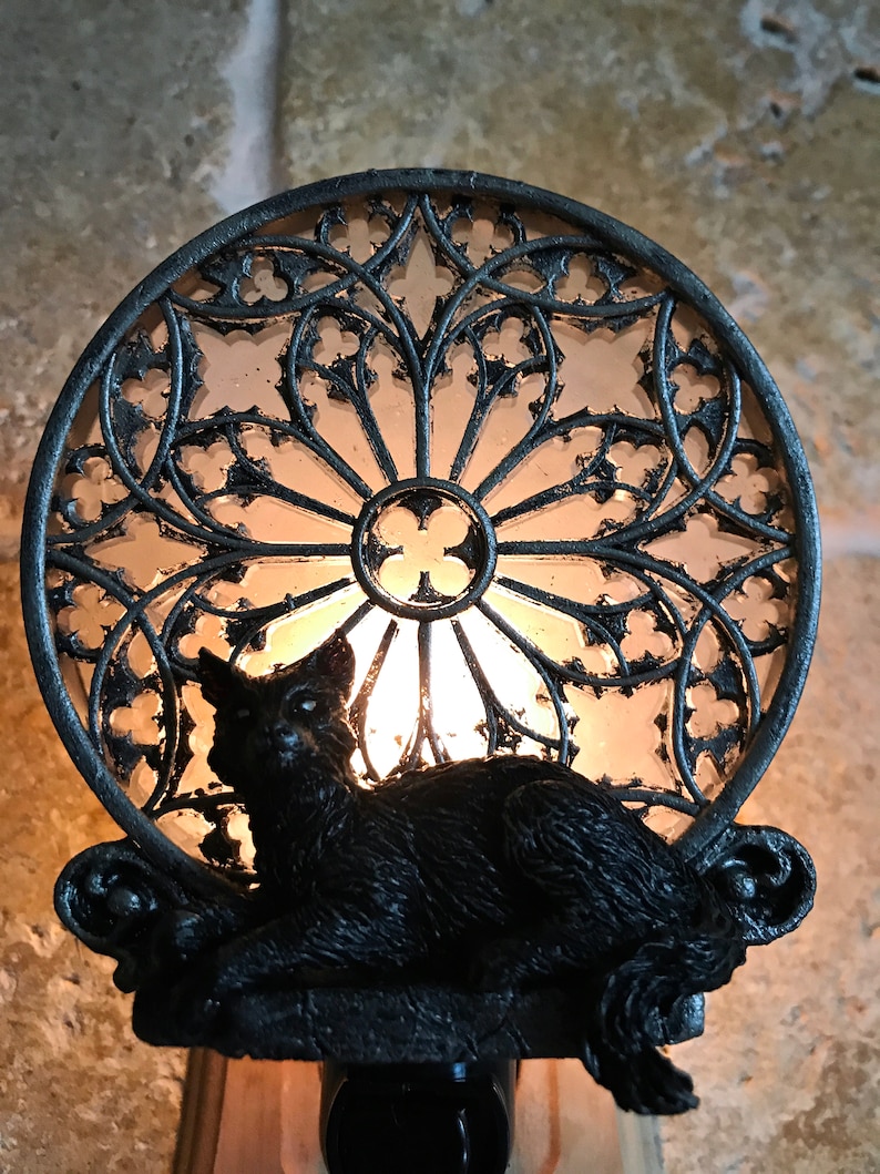 Peut inclure: Une veilleuse en forme de chat noir avec un motif de vitrail. La lumi&egrave;re est allum&eacute;e et le chat est assis devant le vitrail.