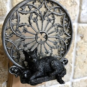 Peut inclure: Une figurine de chat noir est pos&eacute;e sur une base en m&eacute;tal argent&eacute; avec un motif d&eacute;coratif circulaire en vitrail. La base est fix&eacute;e &agrave; un bloc de bois.