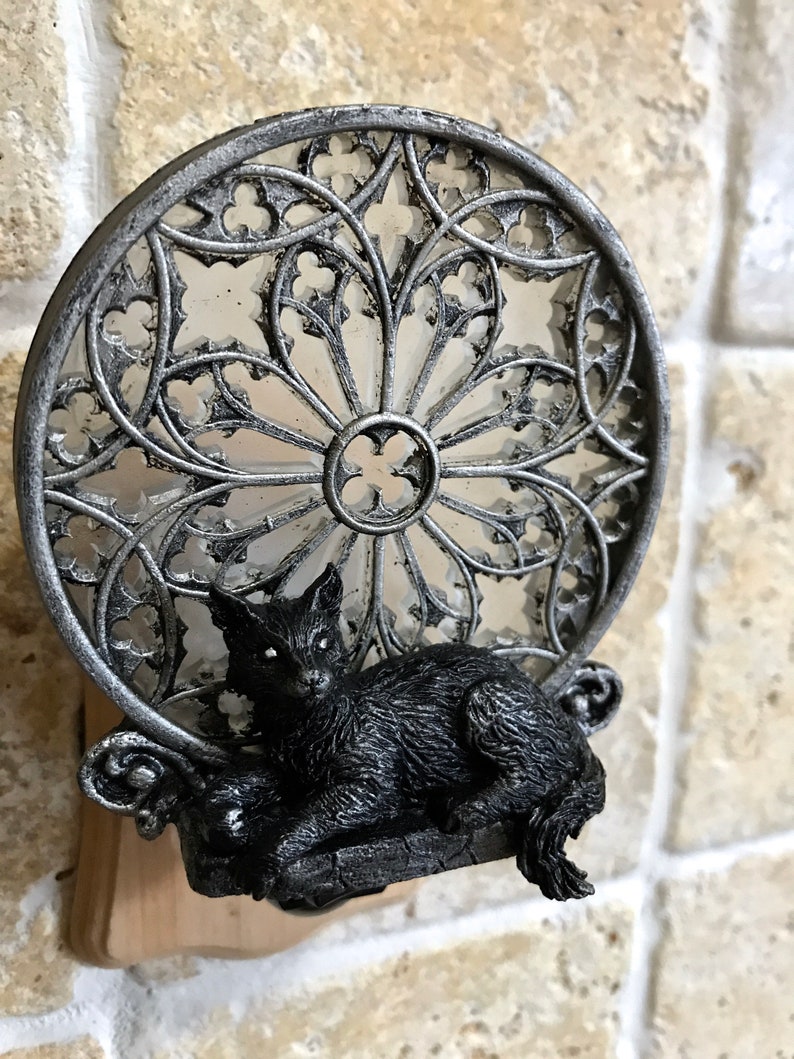Peut inclure: Une figurine de chat noir est pos&eacute;e sur une base en m&eacute;tal argent&eacute; avec un motif d&eacute;coratif circulaire en vitrail. La base est fix&eacute;e &agrave; un bloc de bois.