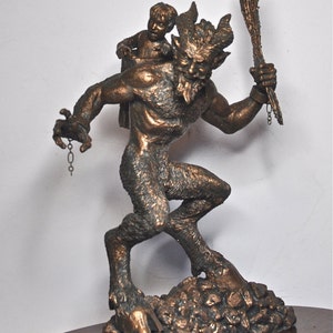May include: A bronze sculpture of a satyr carrying a small child on his back. The satyr is holding a stick in his right hand and a chain in his left hand. The sculpture is set on a base of rocks.