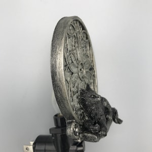 Peut inclure: Veilleuse branch&eacute;e argent&eacute;e et noire avec un chat assis devant une fen&ecirc;tre d&eacute;corative circulaire argent&eacute;e.