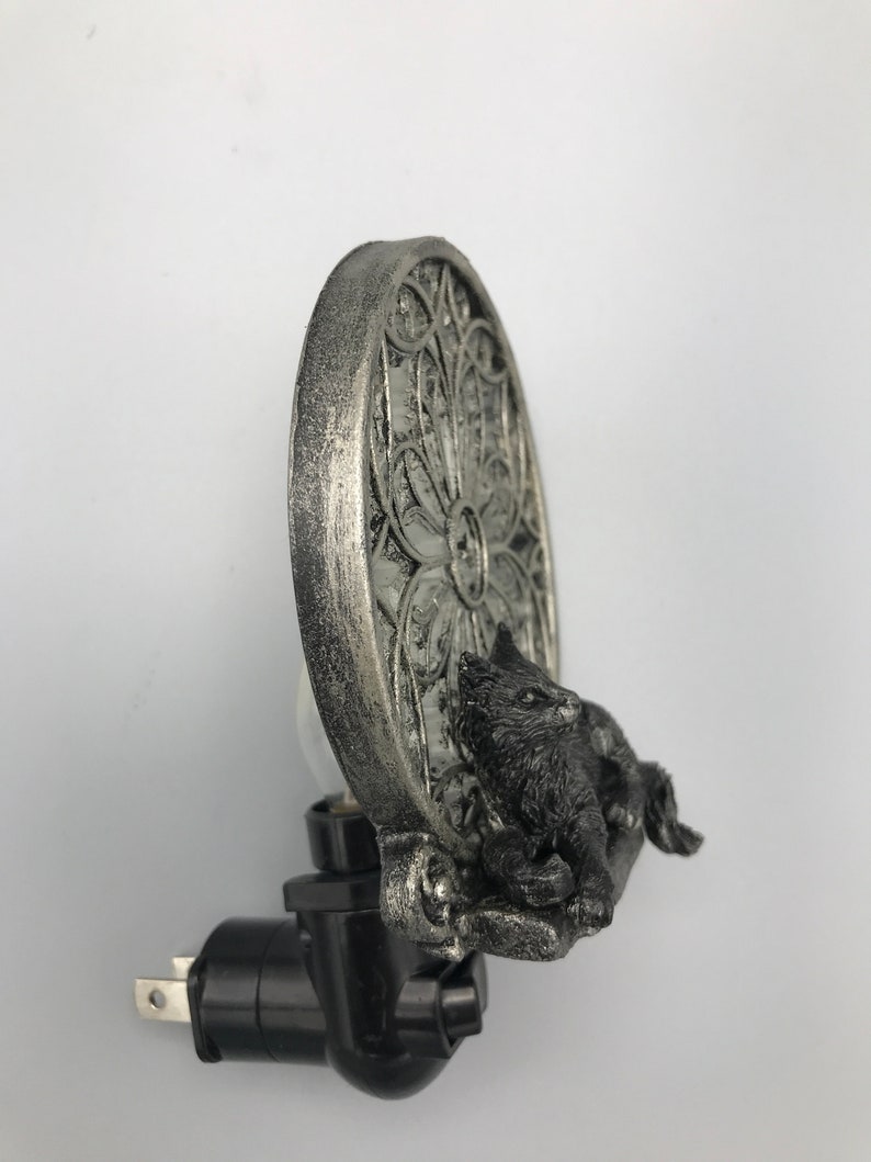 Peut inclure: Veilleuse branch&eacute;e argent&eacute;e et noire avec un chat assis devant une fen&ecirc;tre d&eacute;corative circulaire argent&eacute;e.