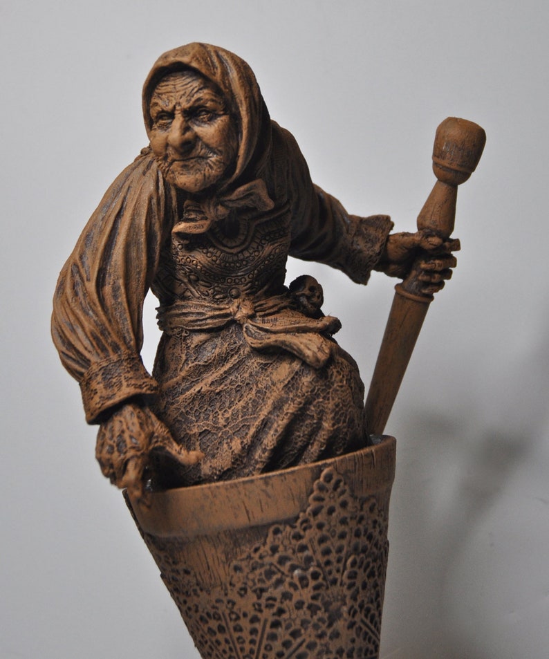 May include: A brown ceramic figurine of a woman holding a mortar and pestle. The woman is wearing a brown dress and a brown head covering. The mortar and pestle are also brown.
