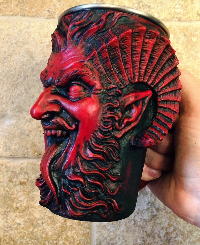 May include: A red and black ceramic mug shaped like a demon's head with a beard and horns. The mug has a detailed design and is perfect for serving beverages.