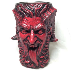 May include: A red ceramic mug shaped like a devil's head with horns, a beard, and a tongue sticking out.