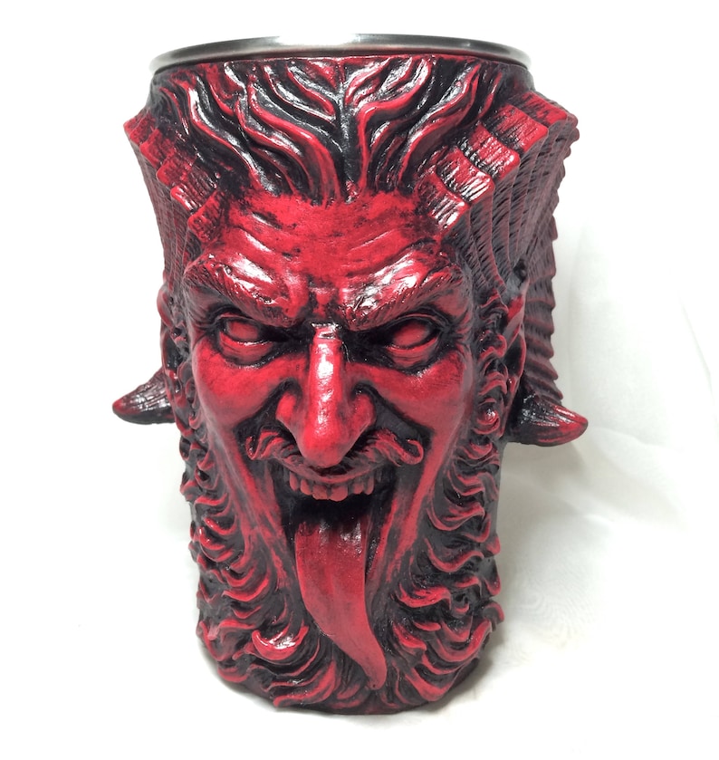 May include: A red ceramic mug shaped like a devil's head with horns, a beard, and a tongue sticking out.