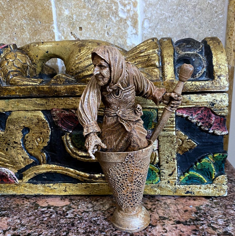 May include: A brown wooden figurine of a woman holding a mortar and pestle. The figurine is standing on a wooden base with intricate carvings.