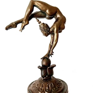 May include: A bronze sculpture of a woman performing a yoga pose, balancing on a ball atop a decorative base.