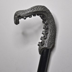 May include: A silver-colored walking stick with an octopus-shaped handle. The handle is detailed with textured skin and suction cups.