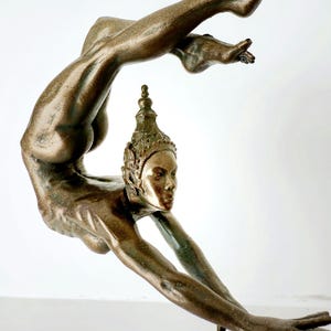 May include: A bronze sculpture of a woman in a contorted pose, with her head tilted back and her arms outstretched. The sculpture is highly detailed, with intricate features on the woman's face and body.