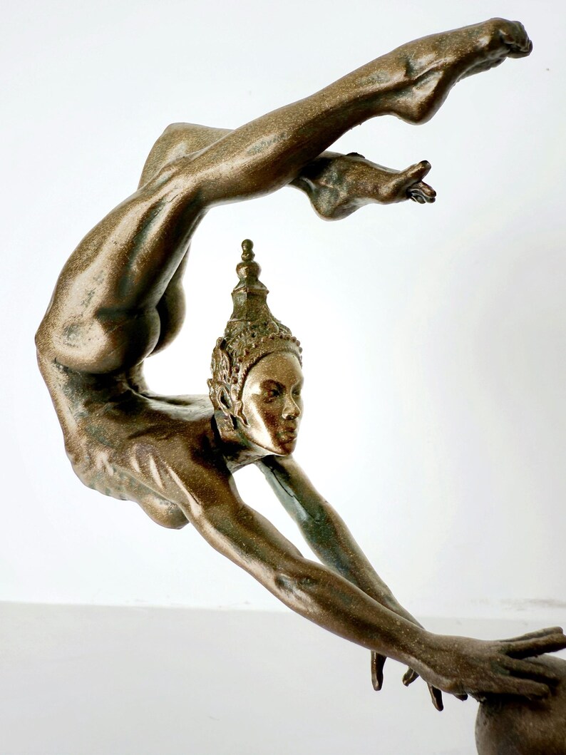 May include: A bronze sculpture of a woman in a contorted pose, with her head tilted back and her arms outstretched. The sculpture is highly detailed, with intricate features on the woman's face and body.