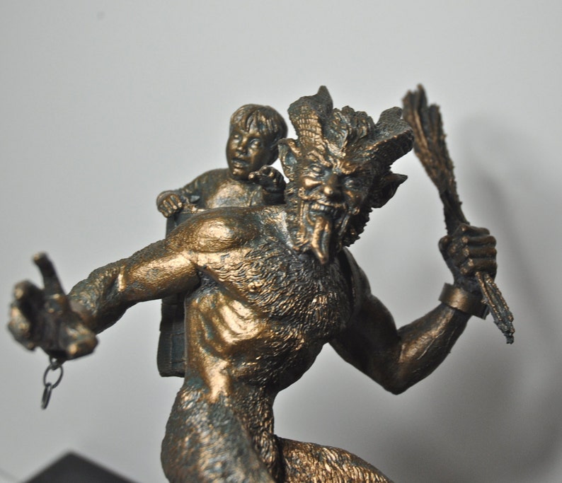 May include: A bronze sculpture of a horned, goat-like creature carrying a small child on its back. The creature has a fierce expression and is holding a staff in its hand.