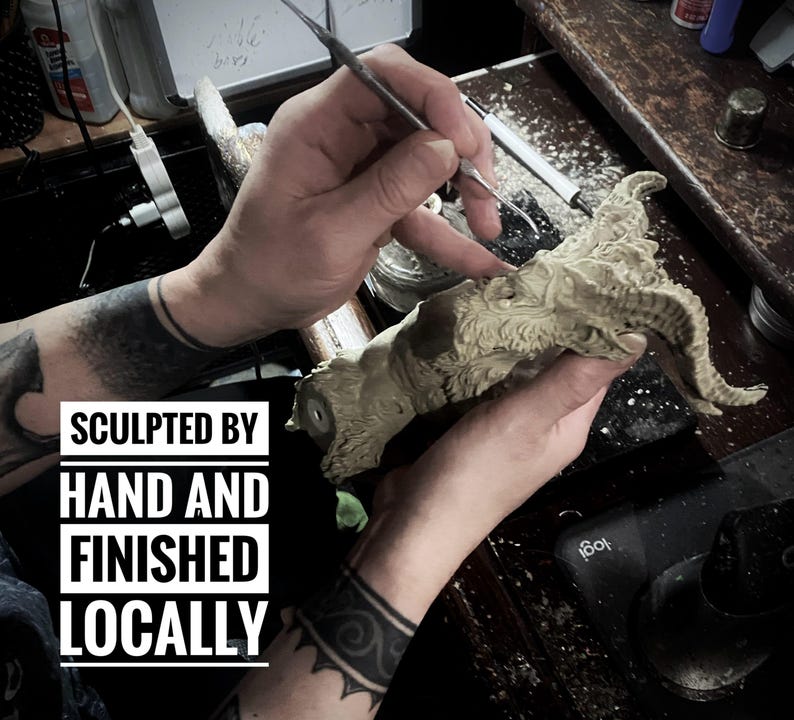May include: A close-up of a person's hands sculpting a detailed, gray, clay sculpture of a creature with horns. The text "SCULPTED BY HAND AND FINISHED LOCALLY" is visible in the image.
