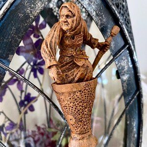 May include: A wooden figurine of a woman with a long white beard and a pointed hat, holding a staff. The figurine is sitting in a wooden cup with intricate carvings.