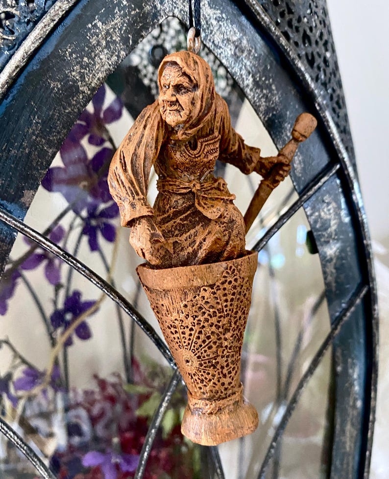 May include: A wooden figurine of a woman with a long white beard and a pointed hat, holding a staff. The figurine is sitting in a wooden cup with intricate carvings.