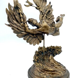 May include: A bronze sculpture of a winged figure with outstretched arms, soaring above a wave base. The figure is depicted in mid-flight, with its wings spread wide and its body tilted forward. The sculpture is mounted on a circular base, which is decorated with a wave design.