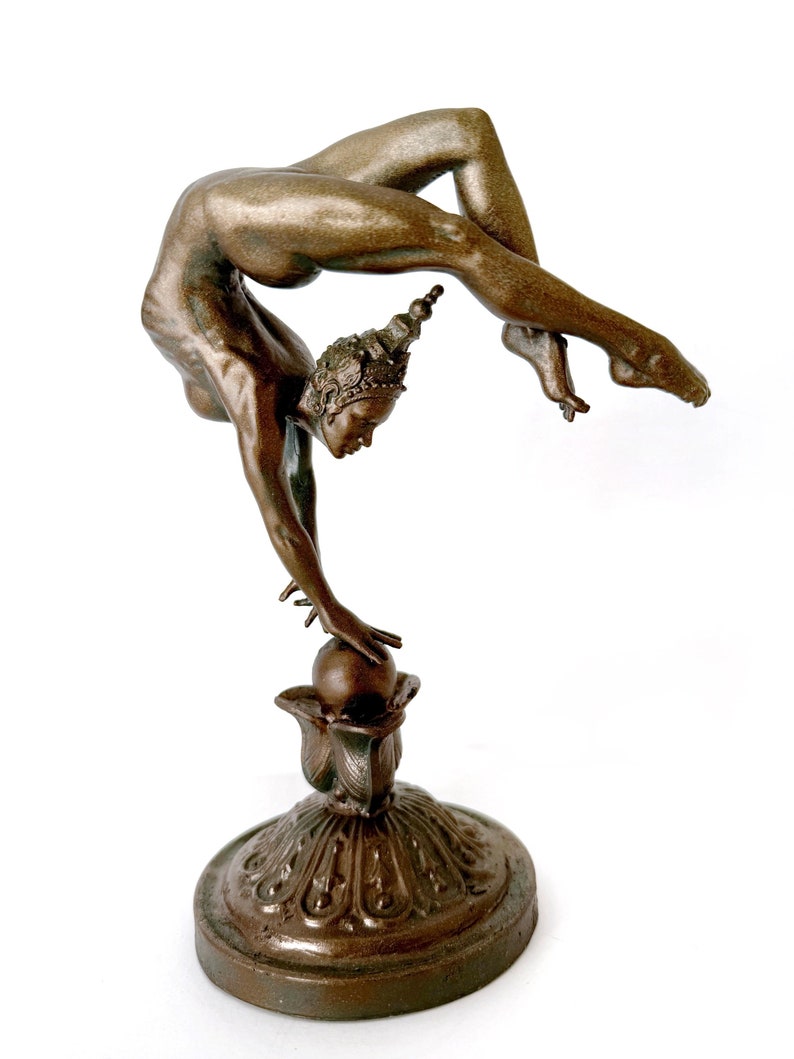May include: A bronze sculpture of a woman balancing on a ball. The woman is in a contortionist pose, with her body bent backwards and her arms outstretched. The sculpture is on a decorative base with intricate details.
