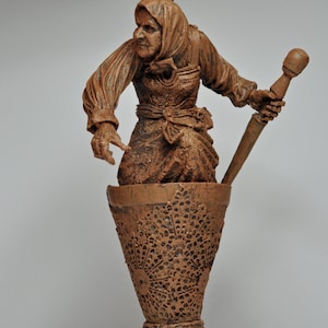 May include: A brown ceramic figurine of a woman holding a mortar and pestle. The woman is wearing a long brown dress and a brown shawl. The figurine is hanging from a black cord.