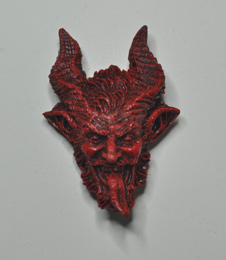 May include: Red devil head sculpture with horns, a beard, and a tongue sticking out. The sculpture is made of a textured material and has a detailed design.