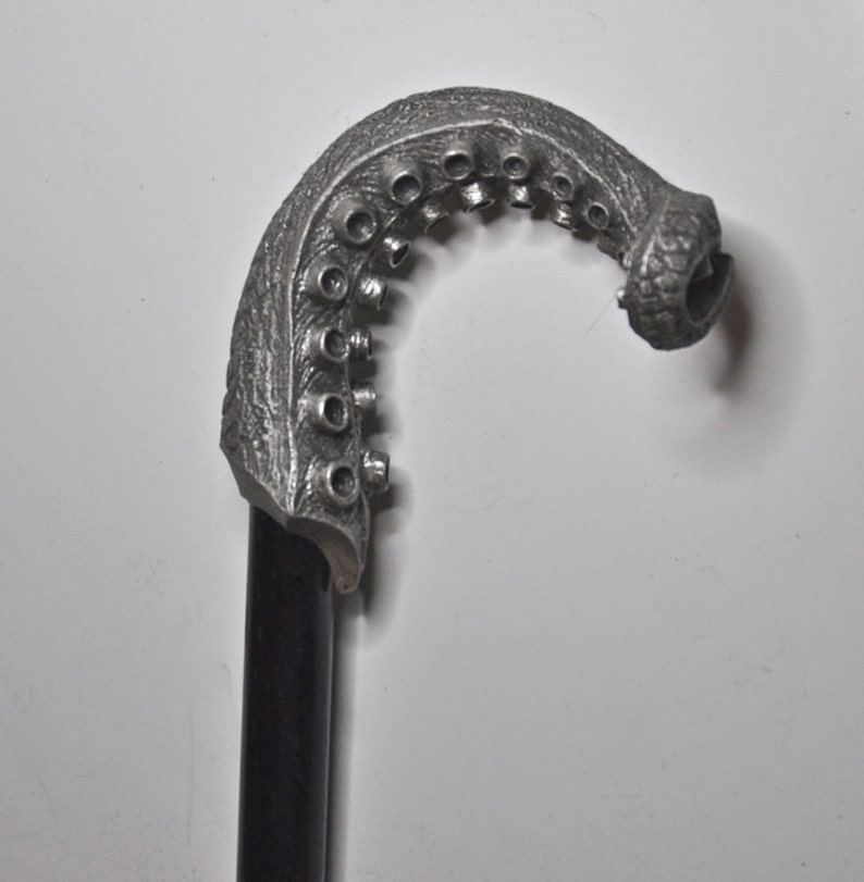 May include: A silver-colored walking stick with an octopus-shaped handle. The handle is detailed with textured tentacles and suction cups.