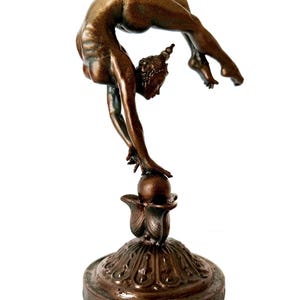 May include: A bronze sculpture of a woman performing a contortionist pose, balancing on a ball atop a decorative base.