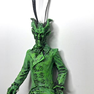 May include: Green and black Christmas ornament of a devilish figure wearing a suit and holding a cane.