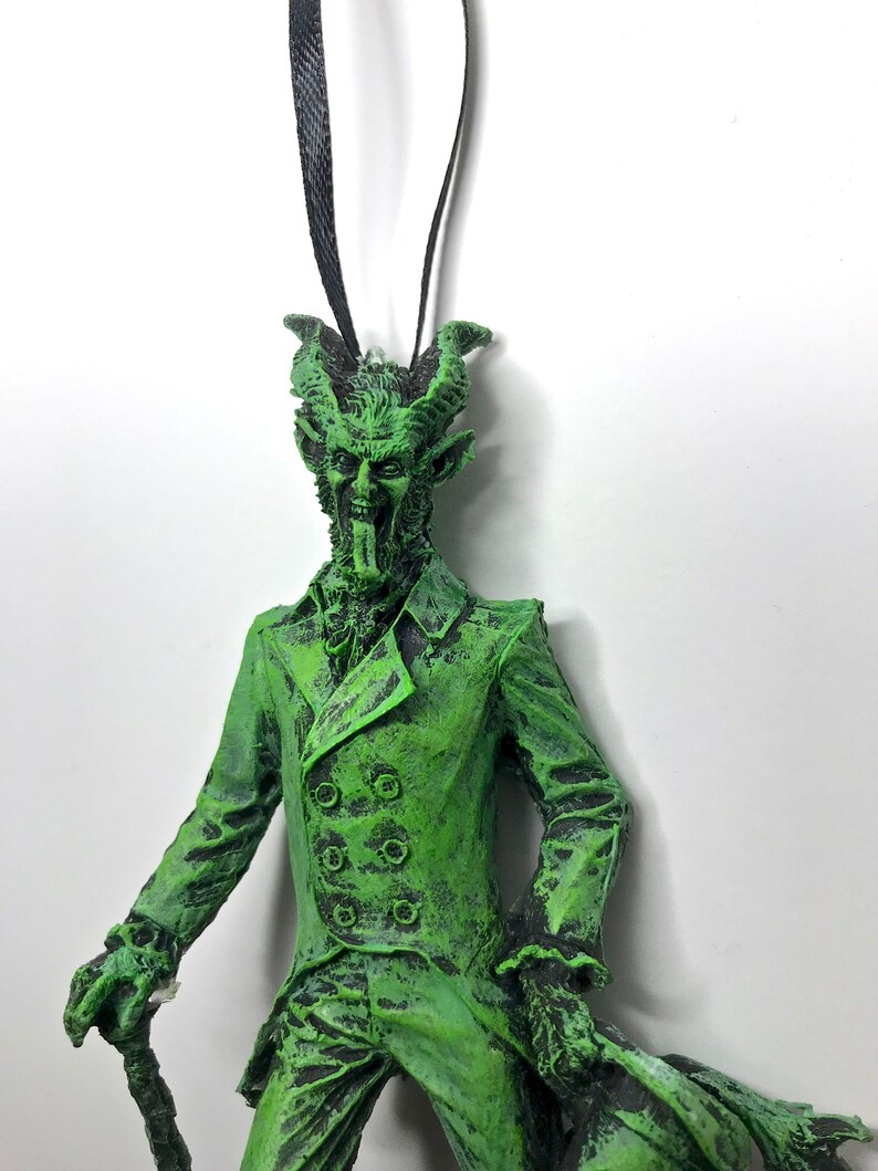 May include: Green and black Christmas ornament of a devilish figure wearing a suit and holding a cane.