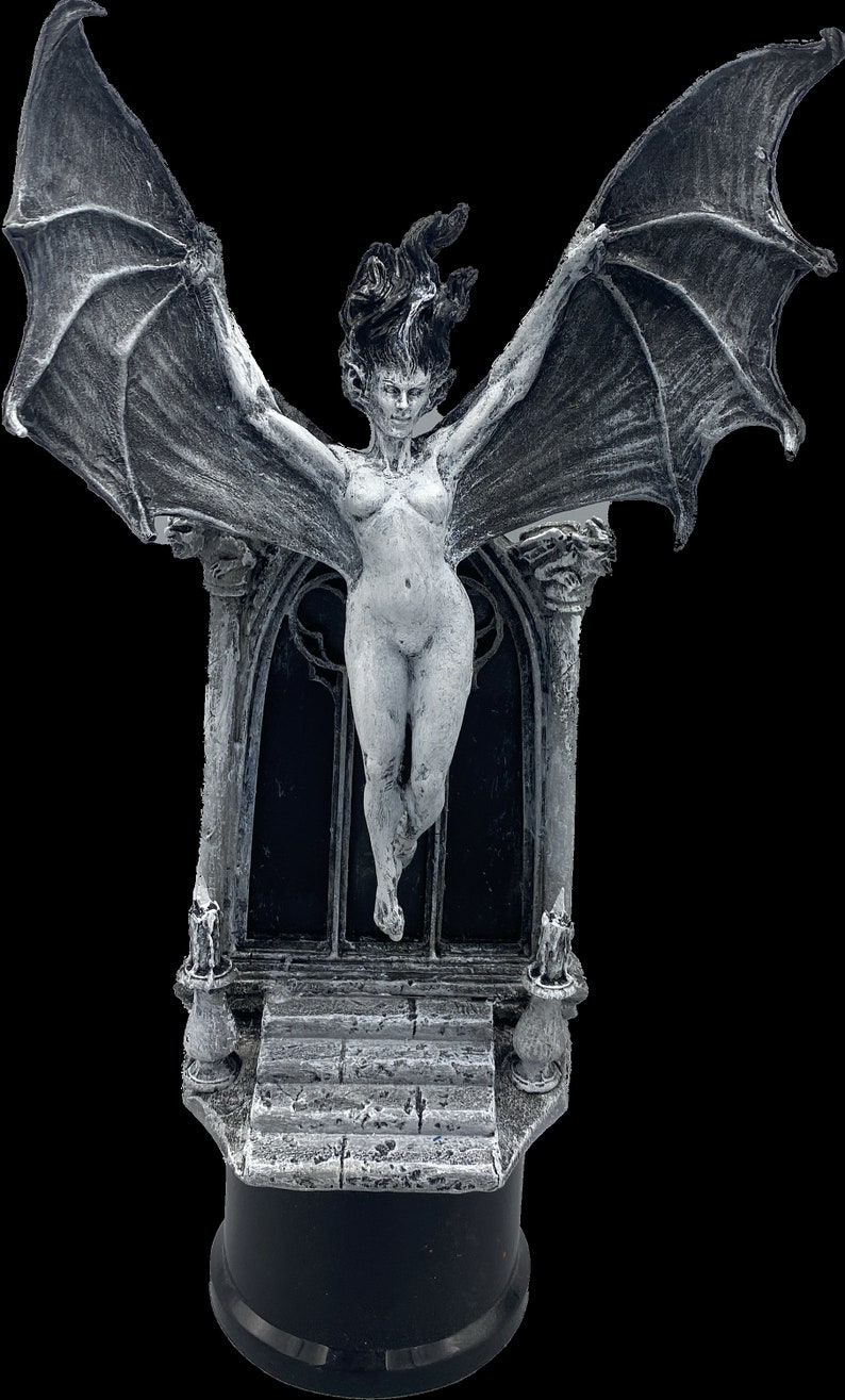 Pode incluir: Uma escultura de uma figura feminina alada branca com cabelo comprido, em p&eacute; sobre uma base de pedra com um arco g&oacute;tico. A escultura &eacute; pintada em um estilo desgastado e envelhecido.