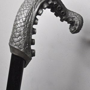 May include: A silver-colored walking stick with an octopus-shaped handle. The handle is detailed with textured skin and suction cups.