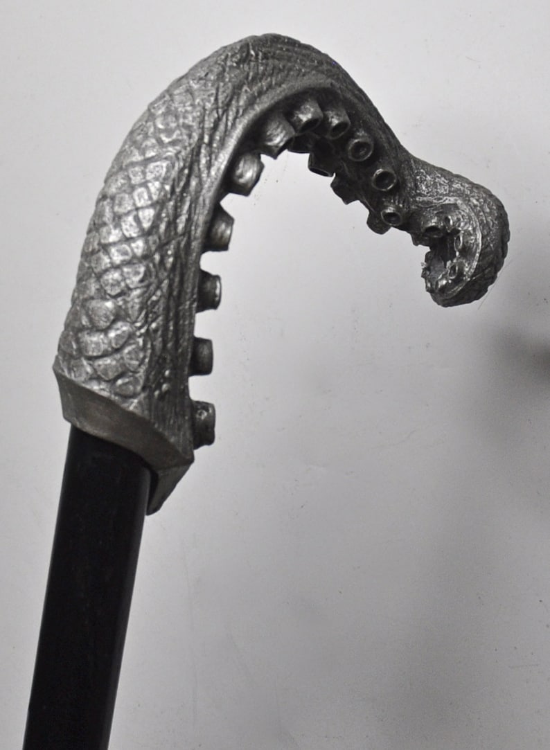May include: A silver-colored walking stick with an octopus-shaped handle. The handle is detailed with textured skin and suction cups.