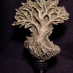 May include: A bronze-colored bottle stopper shaped like a tree with intricate details. The tree has a textured surface and a green patina. The stopper has a metal base with a pointed tip.