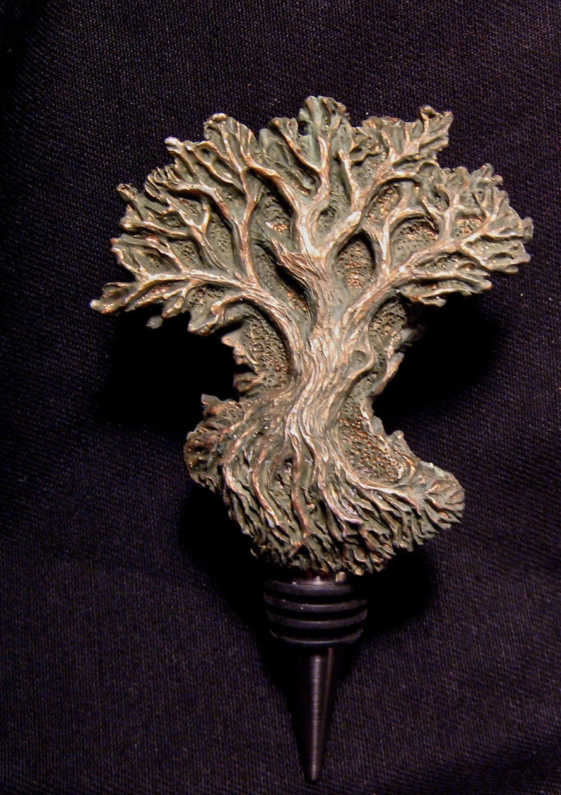 May include: A bronze-colored bottle stopper shaped like a tree with intricate details. The tree has a textured surface and a green patina. The stopper has a metal base with a pointed tip.