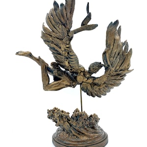 May include: A bronze sculpture of an angel with wings outstretched, falling into a wave. The angel is depicted with a human body and feathered wings. The sculpture is mounted on a base that resembles a wave.