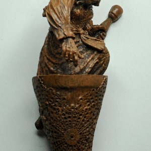 May include: A brown ceramic figurine of a woman holding a broom, sitting on a brown, lacy base. The figurine is a Christmas ornament.