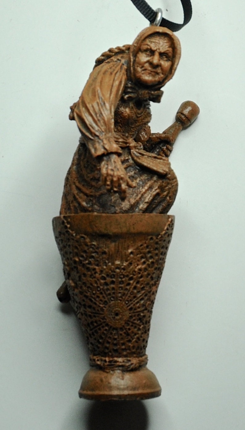 May include: A brown ceramic figurine of a woman holding a broom, sitting on a brown, lacy base. The figurine is a Christmas ornament.