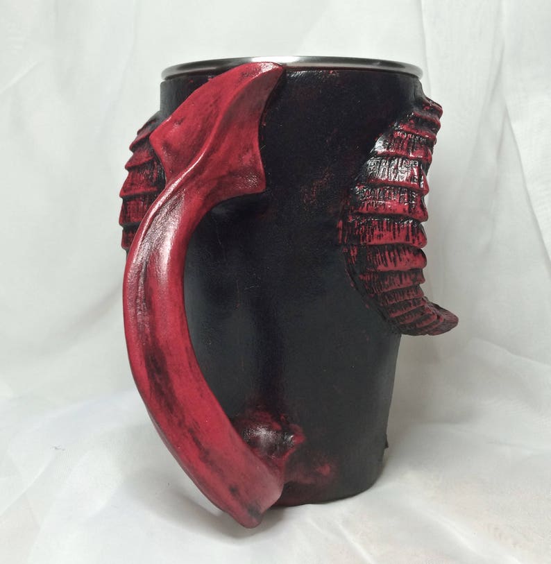 May include: A black and red ceramic mug with a dragon-shaped handle. The mug has a textured surface and a stainless steel rim.