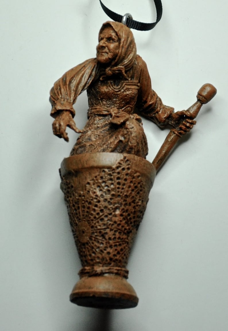 May include: A brown ceramic figurine of a woman holding a wooden pestle. The woman is wearing a long brown dress and a brown head covering. The figurine is sitting in a brown ceramic mortar.