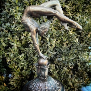 May include: A bronze sculpture of a woman performing a handstand on a ball. The sculpture is on a decorative base with intricate details.