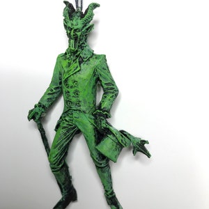 May include: Green, devil-like ornament with horns, a top hat, and a cane. The ornament is made of plastic and has a distressed paint finish.