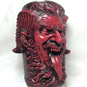 May include: Red ceramic mug shaped like a demon's head with a long tongue sticking out. The mug has a stainless steel rim.