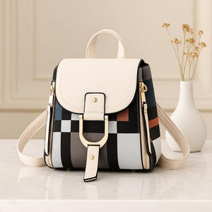 May include: A cream-colored backpack with a flap closure and a top handle. The front of the backpack features a geometric pattern in black, gray, and brown. Gold-colored zippers and hardware add a touch of elegance. The straps are cream-colored.