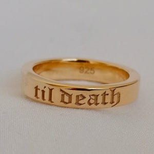 Könnte beinhalten: Ein goldfarbener Ring mit der Inschrift "til death" in einer altenglischen Schriftart. Der Ring hat eine glatte, polierte Oberfläche und die Nummer "925" ist sichtbar. Der Ring ist wahrscheinlich aus Sterlingsilber.