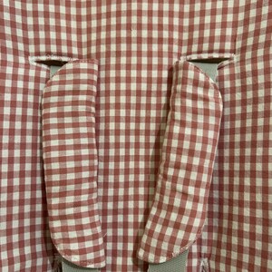 May include: Close-up of a baby high chair seat cover. The cover features a red and white gingham pattern. Two padded armrest covers are visible, along with gray straps for securing the child. The fabric is a soft, woven material.