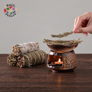 May include: A brown ceramic oil burner with a lit tea light candle inside, topped with a bowl containing dried herbs. Beside it are two bundles of dried sage and cedar wrapped in white string. The logo Knit Future is visible in the corner.