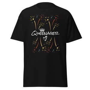 May include: Black t-shirt with a graphic design featuring the word "Queenagerz" in white script, a crown, and a heart. The design includes colourful firework-like bursts in yellow, red, and blue.
