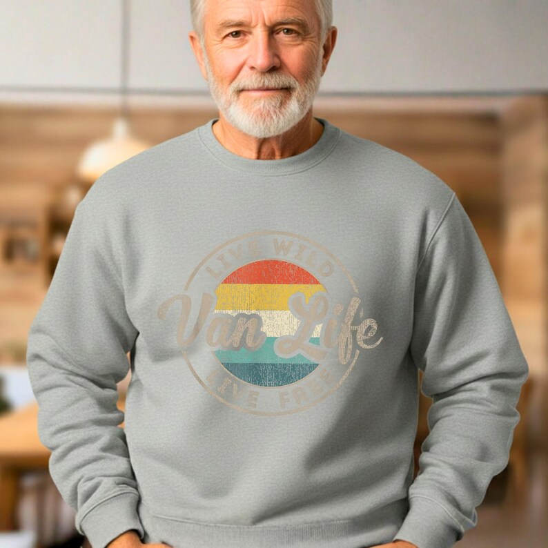 May include: A light gray sweatshirt with a circular graphic that reads "Van Life" in a vintage style. The graphic features a retro sunset design with red, yellow, and blue stripes. The text "Live Wild, Live Free" is also included.