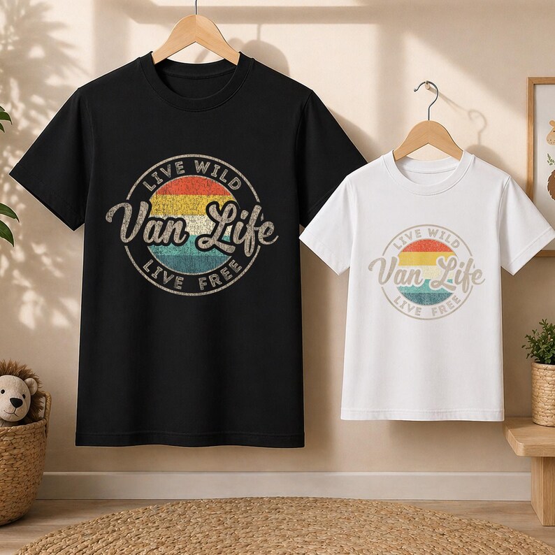 May include: Two t-shirts, one black and one white, each with a circular graphic. The graphic reads "Live Wild Van Life Live Free" in a vintage style, with a colorful sunset design. Both shirts are short-sleeved.