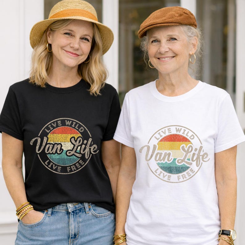 May include: Two women wearing black and white t-shirts with a circular graphic. The graphic reads "Live Wild Van Life Live Free" in a vintage style with a rainbow color scheme. Both are wearing hats and smiling.