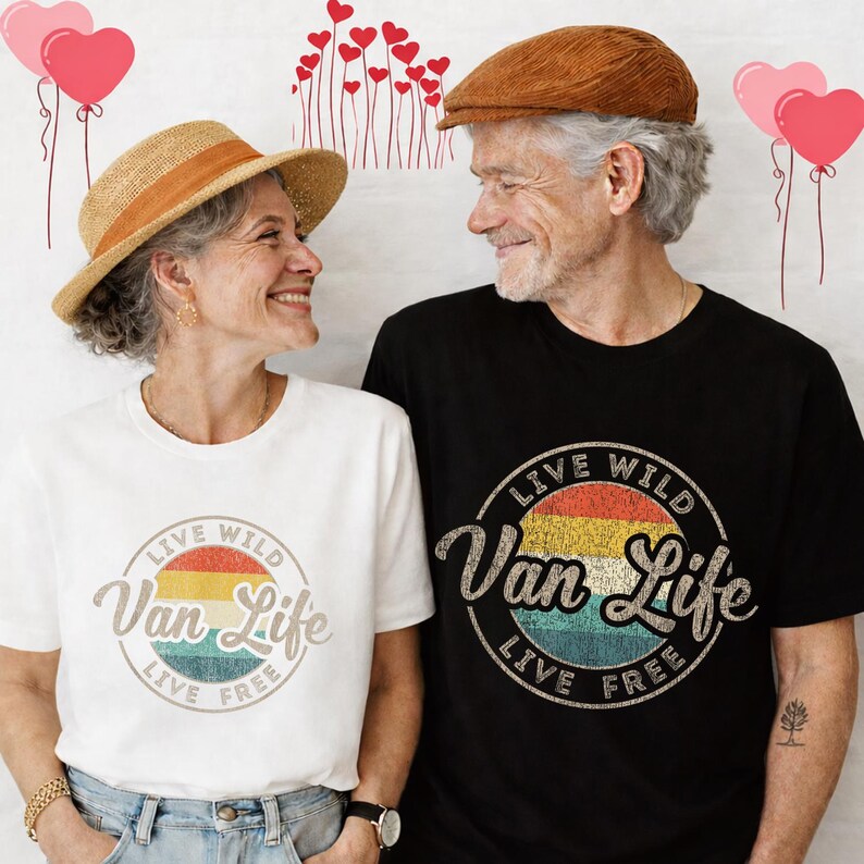 May include: A couple wearing matching t-shirts with a "Live Wild Van Life Live Free" design. The woman wears a white shirt and a straw hat. The man wears a black shirt and a brown cap. The design features a retro sunset color scheme.